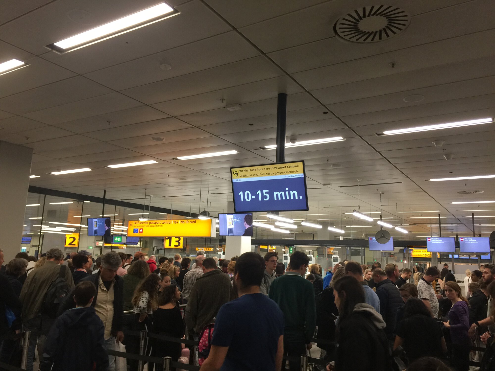People staying in line for passport control, monitor above shows approximate wait time: 10-15 minutes